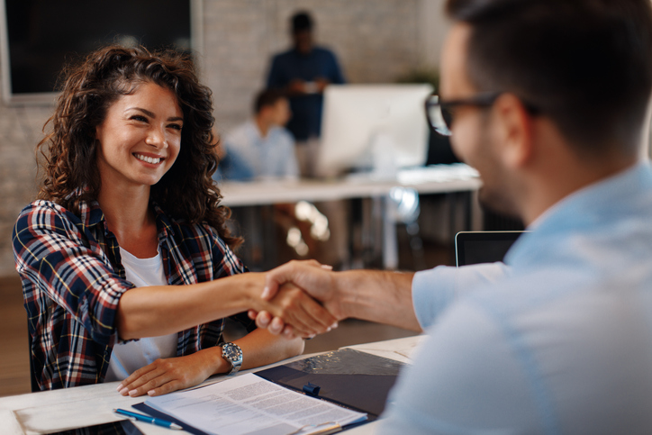 A candidate for a job smiles with confidence and shakes the interviewers hand.